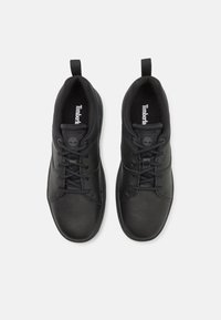 Zapatillas de cuero negras con una textura suave, punta redondeada, suela de goma y diseño de cordones lateral. Presenta una pestaña en el bucle para ponerlas con facilidad.