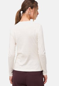 Top a maniche lunghe di colore crema realizzato in un tessuto morbido, con scollo rotondo e vestibilità rilassata. Tessuto liscio con un design semplice.