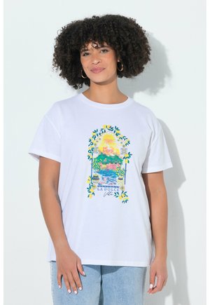 Kobieta o kręconych włosach, ubrana w białą koszulkę z kolorowym śródziemnomorskim pejzażem z cytrynami i napisem „La Dolce Vita”.