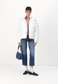 Witte pufferjack met hoge kraag, lichtroze top, blauwe schoudertas, cropped blauwe jeans en zwarte loafers met witte sokken.