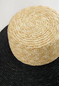 Rund vävd korg gjord av naturfiber, med en ljusbrun topp och en svart botten, samt en strukturerad flätad design.
