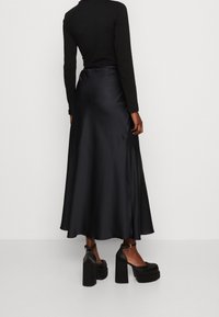 Jupe maxi en satin noir avec une silhouette fluide, présentant une texture lisse et un éclat subtil. Associée à des compensées noires chunky.