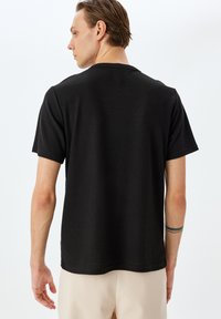 Sort t-shirt med korte ærmer, tekstureret mønster, rund halsudskæring og en afslappet pasform. Bæres med lyse bukser, der viser en subtil designdetalje.