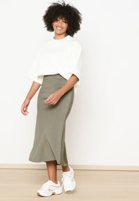White oversized sweatshirt with short sleeves, paired with a fitted olive green midi skirt and white sneakers with beige accents.