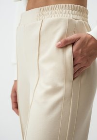 Pantalons beiges à taille élastique avec poches latérales, dotés de coutures verticales et d'un tissu doux et texturé.