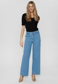 Jean larges taille haute de couleur bleu clair avec une fermeture à boutons et à zip, associée à un haut noir ajusté à côtes. Texture denim lisse.