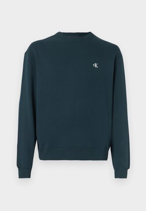Mörkgrön sweatshirt med rund hals i bomull med långa ärmar, ribbade muddar och en liten vit logotyp på bröstet. Mjuk textur.