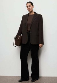 Blazer marrón oversize con solapas, combinado con una blusa marrón ajustada y pantalones de campana negros. Se lleva un bolso marrón a juego.