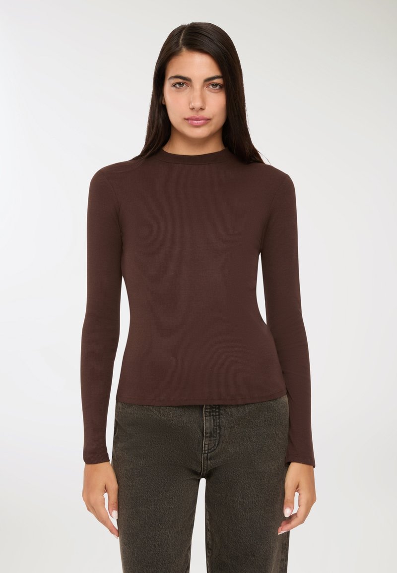 Brązowa, długorękawowa bluzka z ribbowym splotem, o wysokim kołnierzu, dopasowanym kroju i miękkiej fakturze, zestawiona z ciemnoniebieskimi dżinsami.