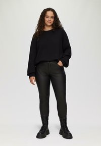 Zwarte oversized trui met een textuur van gebreid patroon, gecombineerd met slanke zwarte nep leren broek en zwarte veterschoenen voor combat.