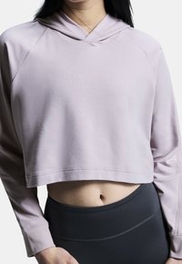 Světle růžová zkrácená mikina s měkkou texturou, se kapucí, raglánovými rukávy a rovním lemem. Nosí se s černými legínami s vysokým pasem.