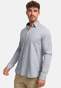 Camisa de manga larga gris claro con cuello de solapas, cierre de botones y una textura suave. Presenta un detalle de color contrastante en el interior del cuello.