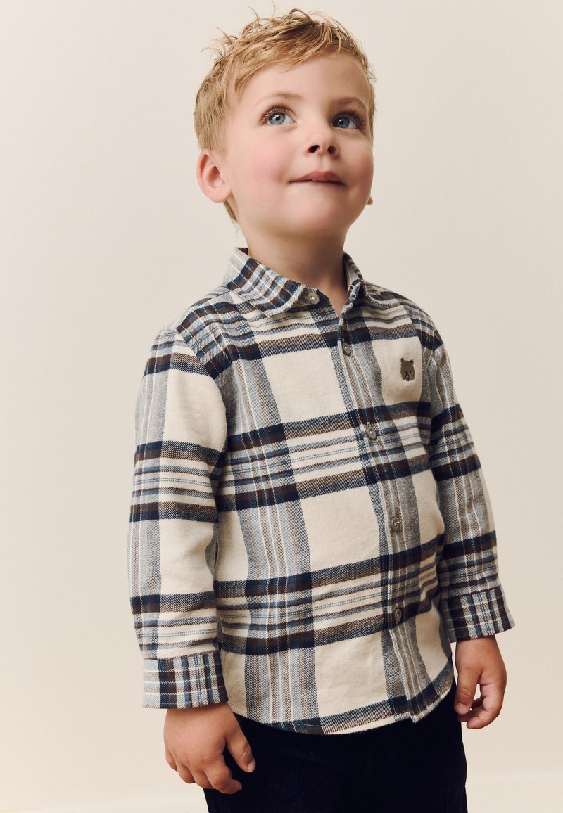 Langärmeliges Flanellhemd in Beige, Blau und Braun; mit Knopfleiste und kleinem Bärenaufnäher auf der Brust.