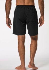 Bañador negro con cintura elástica. Cuenta con un bolsillo trasero y una textura suave. Se lleva sobre un torso desnudo, mostrando las piernas.