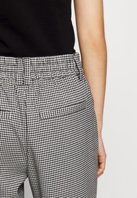 Svart- och vitrutigt mönstrade byxor i houndstooth med avspänd passform, elastisk midja och sidofickor, visade från baksidan.