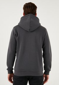 Siva dukserica s velikom, strukturiranom kapuljačom. Ima duge rukave i rebrasti rub. Glatka tekstura, napravljena od mekane tkanine, bez vidljivih logotipa.