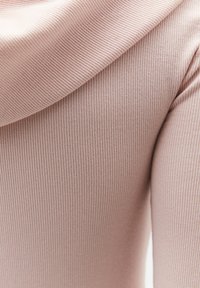 Lyserødt ribstrikket stof med et foldet afsnit, der viser tæt på tekstur og fine lodrette linjer.