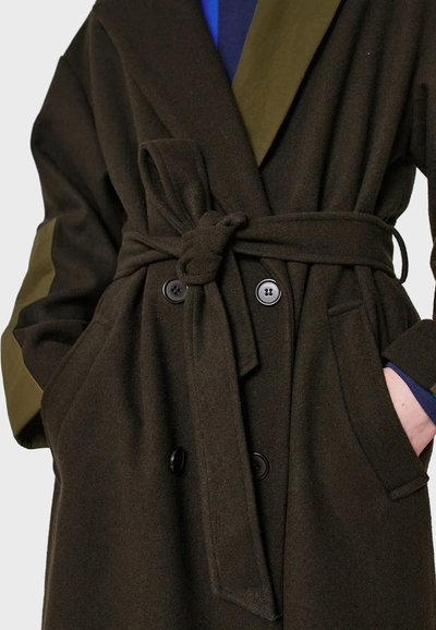 Dark olive wool coat with a belted waist, large lapels, two front pockets, and black button closures. Contrast green collar accents.