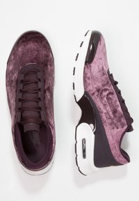 Scarpe Nike in velluto viola scuro, con una superficie testurizzata, dettagli neri e una suola in gomma bianca. Un'unità Air visibile sul tallone.