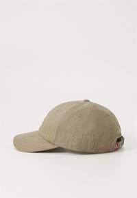 Khaki cap med strukturert stoff, buet skygge og justerbar stropp bak. Har ventilasjonsoller og en logodetalj på siden.