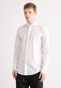 Witte lange mouwen shirt van soepel katoen, met een klassieke kraag, knopen aan de voorkant en een afgeronde zoom. Draag het met donkere broeken.