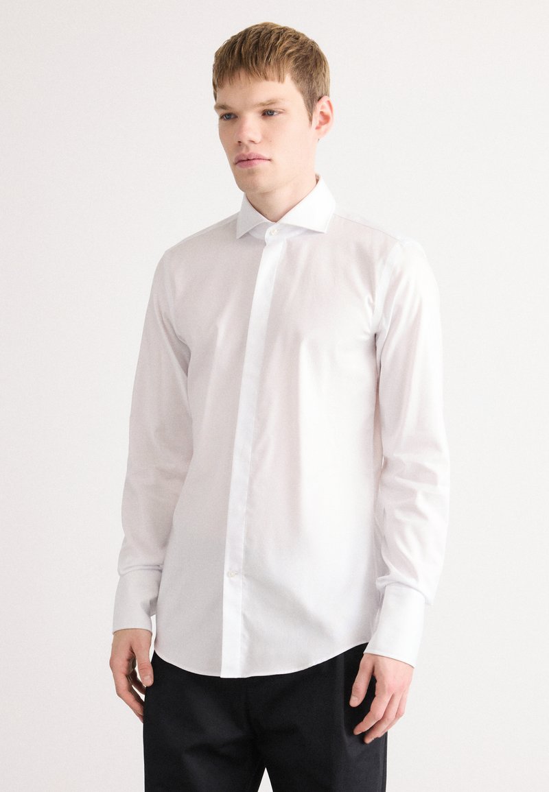 Witte lange mouwen shirt van soepel katoen, met een klassieke kraag, knopen aan de voorkant en een afgeronde zoom. Draag het met donkere broeken.