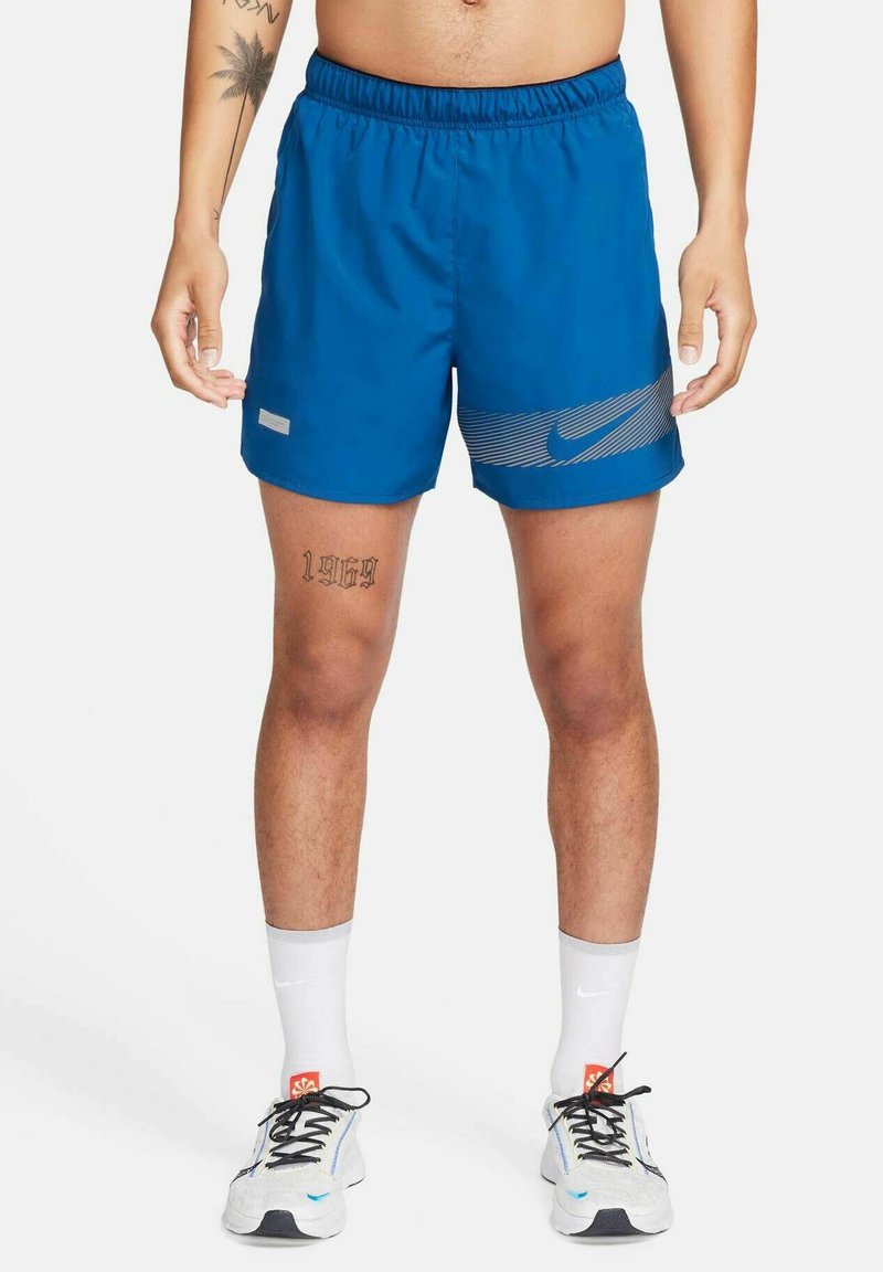 Pantalones cortos Nike azules con cintura elástica, que presentan un patrón de rayas plateadas cerca del dobladillo. Combinados con calcetines blancos y zapatillas deportivas multicolores.