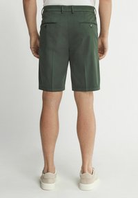 Gröna shorts i lätt tyg, med två bakfickor med dragkedjor och en ren fåll. Bärs med ljusa sneakers.