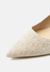 Κοντινό πλάνο μιας μπεζ μυτερής γόβας με υφασμάτινη υφή που φέρει ένα λεπτό γεωμετρικό μοτίβο και λείο εσωτερικό επένδυση.