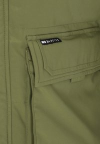 Olivengrønt stof med en glat tekstur, med en klaplomme og et sort mærke med teksten "MO Arctic." Enkel, funktionel design.