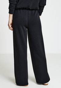 Schwarze, weit geschnittene Jogginghosen aus weichem Material mit elastischem Bund. Das Design legt Wert auf Komfort und Bewegungsfreiheit.