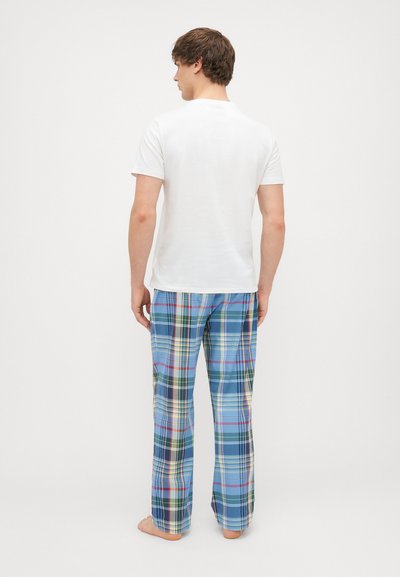 Balts īsām piedurknēm T-krekls kopā ar ziliem svītrainiem mājas biksēm ar zaļiem, dzelteniem un sarkaniem akcentiem. Mīksts audums, brīva piegriezums.