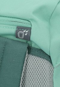 A textured mint green backpack section with a gray zipper and a logo patch featuring a paw print, showcasing durable fabric and breathable mesh.
