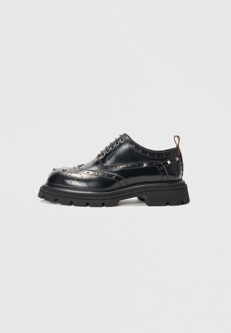 Pantofii oxford din piele neagră au detalii decorative cu cuie, talpă groasă din cauciuc și ochiuri metalice pentru șireturi. Vârful este conic, iar în călcâi se află un tab pentru a-i trasa.