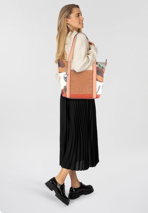 Bolso tote con un cuerpo de lona de patrón multicolor y base de cuero texturizado marrón. Presenta asas dobles y un llavero decorativo.