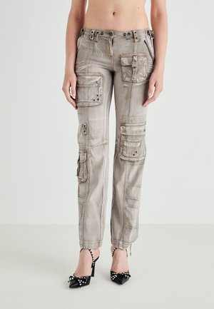 Osoba nosząca jasnoszare spodnie bojówki z wieloma kieszeniami oraz czarne szpilki ozdobione perłowymi dekoracjami.