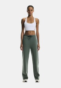 White cropped tank top paired with loose-fitting, dark green sweatpants featuring an adjustable drawstring. Smooth fabric with subtle texture.