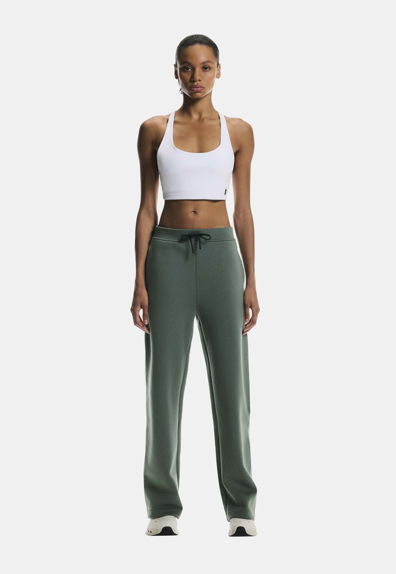 White cropped tank top paired with loose-fitting, dark green sweatpants featuring an adjustable drawstring. Smooth fabric with subtle texture.