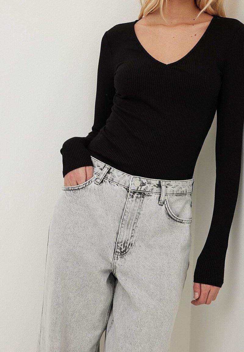 Černý žebrovaný top s dlouhým rukávem a výstřihem do V, v kombinaci s světle šedými širokými džíny s vysokým pasem, které mají vybledlý vzhled a boční kapsy.
