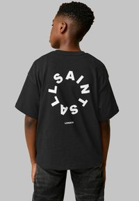 Juodas medvilninis marškinėlis su ryškiu baltu užrašu "SAINT LAURENT LONDON" apvalioje sąsajoje ant nugaros. Trumpi rankoviai, laisvas kirpimas.
