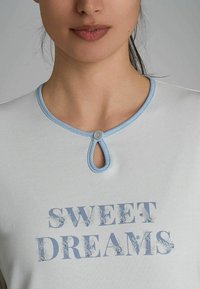 Tunique azzurra chiara con scollo rotondo, un bottone decorativo e un dettaglio a oblò, stampata con la scritta "SWEET DREAMS" in lettere testurizzate.