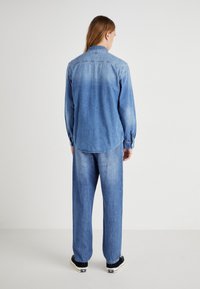 Jasnoniebieska koszula dżinsowa z długimi rękawami i spiczastym kołnierzykiem. Noszona z dopasowanymi, luźnymi jasnoniebieskimi dżinsami i czarnymi trampkami.