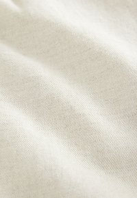 Tissu en coton beige clair avec une texture lisse, présentant un motif discret de tissage diagonal et de légères variations de couleur.