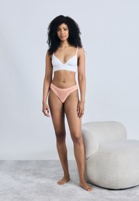 Soutien-gorge léger blanc et string rose avec accents en dentelle et pois. Tissu lisse et détails en dentelle délicate. Fond neutre.