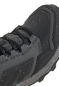 Czarna sportowa buty z teksturowaną cholewką z siateczki, gumową podeszwą oraz wodoodpornymi detalami z kroplami na powierzchni.