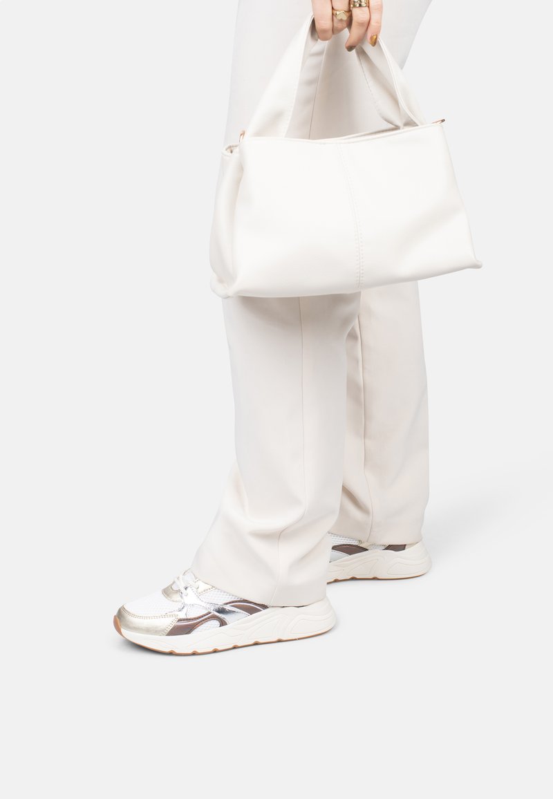 Weiße Leder-Shopper-Tasche mit weicher Struktur, kurzen Griffen und Reißverschluss. Kombiniert mit hellen Hosen und Sneakers mit silberfarbenen Akzenten.
