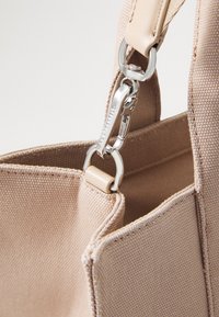 Beige lærredstaske med en struktureret overflade, der har sølvhardware og en holdbar remmontering.