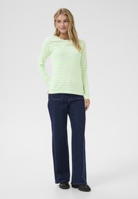 Maglietta a maniche lunghe verde chiaro e bianca a righe abbinata a jeans dritti blu scuro e scarpe nere, su uno sfondo neutro.