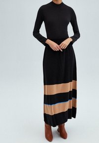 Top negro de manga larga combinado con una falda negra con rayas horizontales en marrón y azul. Largo hasta la rodilla, de tela suave y textura plisada.