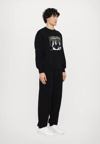 Black sweatshirt featuring a graphic print on the front. Paired with matching black sweatpants and white sneakers, standing against a white background.